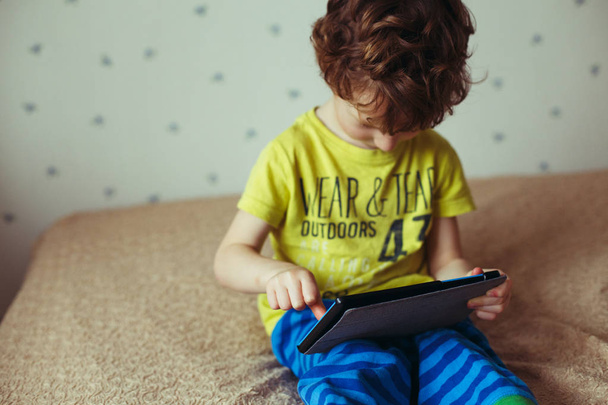 Little cute boy in a green T-shirt playing games on a tablet and watching cartoons. Toddler with tablet. - Foto, immagini