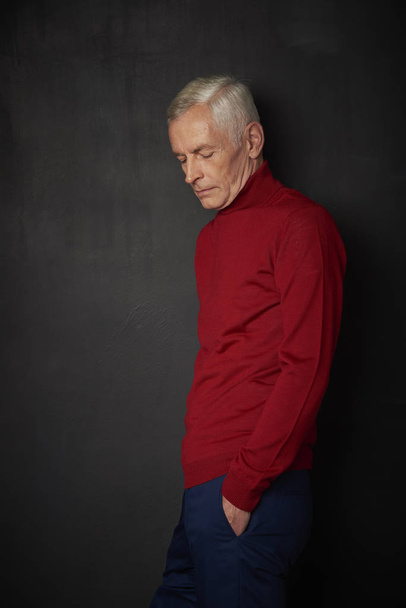 Studio shot of handsome mature man in red turtle neck sweater before dark wall - Photo, Image