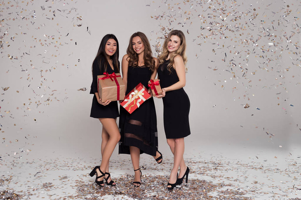 drei schöne Mädchen in schwarzen Kleidern halten und zeigen Schachteln mit Geschenken.  - Foto, Bild