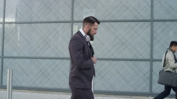4K Laid back bearded businessman wearing headphones as he walking to work - Filmati, video