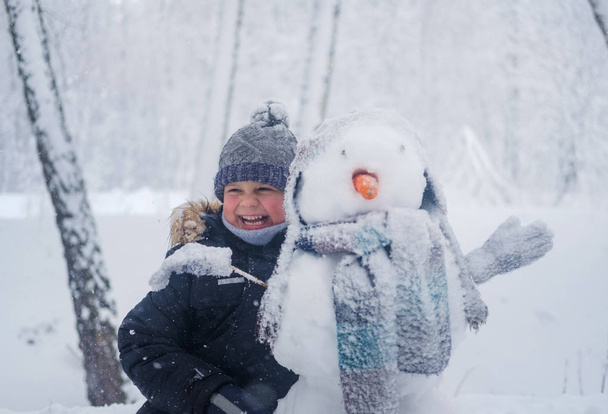 European boy and the snowman in a snowy forest - Фото, изображение