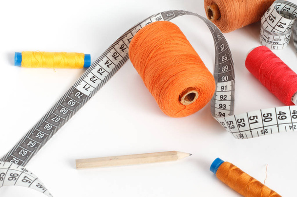 Accessories for sewing: thread, a pencil and a centimeter on a white background. Orange, brown and red bobbin thread. - Photo, image