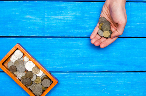 money in hand, casket with coins on a blue wooden background, space for text - Foto, Bild