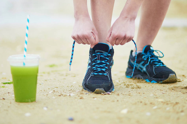 Jogger with green vegetable smoothie, tying sport running shoes laces - Foto, afbeelding