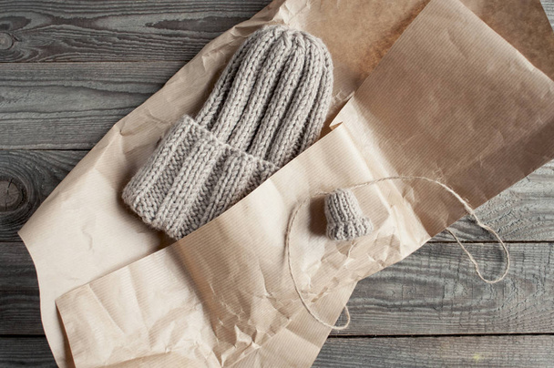 Knitted beige hat  packs in kraft paper with a small sample flat lay on wooden boards. - Foto, Bild