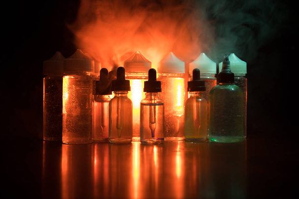 vape Konzept. Rauchwolken und Dampfflaschen auf dunklem Hintergrund. Lichteffekte - Foto, Bild