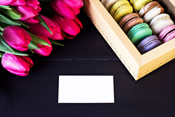 Caja con macarrones y un ramo de tulipanes y una tarjeta para tu texto sobre un fondo oscuro
.  - Foto, imagen