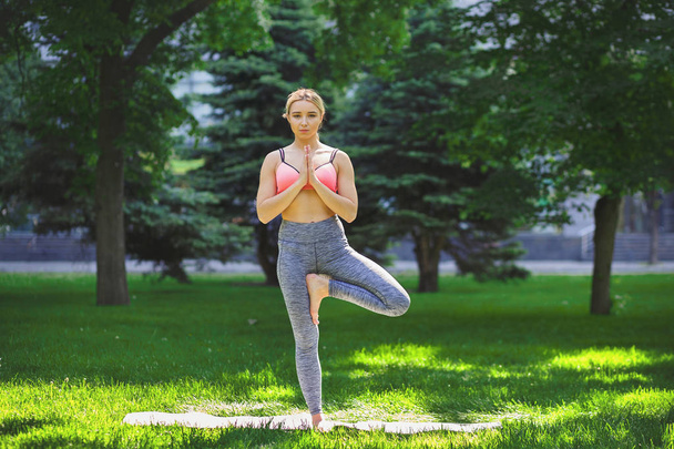 Woman training yoga in tree pose outdoors - Photo, Image