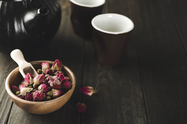 Рожеві бруньки чай на дерев'яній мисці з чайним горщиком
 - Фото, зображення