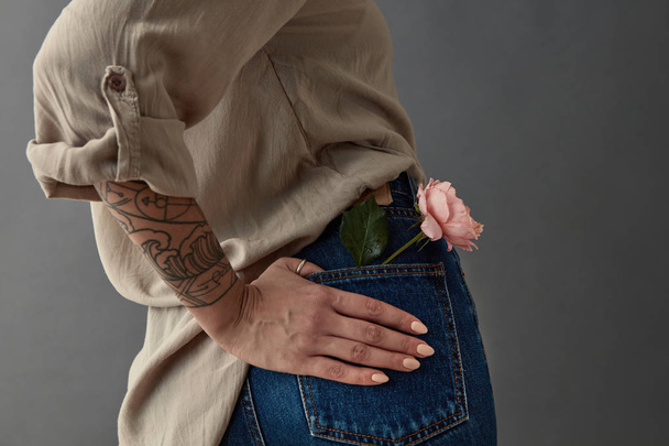 woman in blue jeans with pink rose in back pocket against grey background, Mother's Day, Valentine's Day concept - Foto, imagen