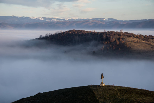 Een christelijk kruis op een heuveltop met uitzicht op een mistige vallei hieronder - Foto, afbeelding