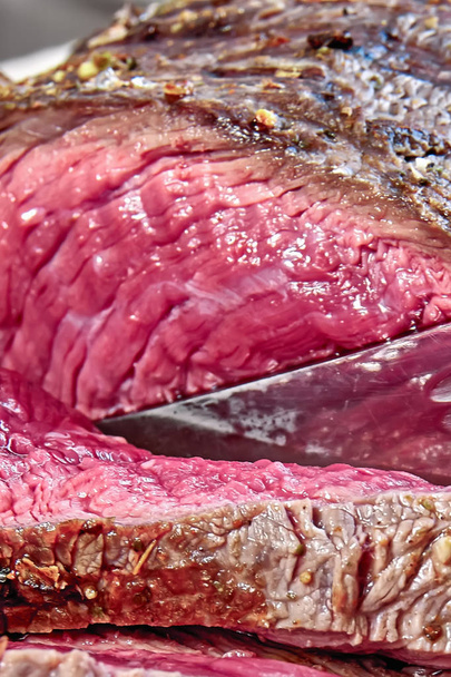 Fried meat with blood is cut with hunting knife. Well done steak closeup. Rustic style. - Φωτογραφία, εικόνα