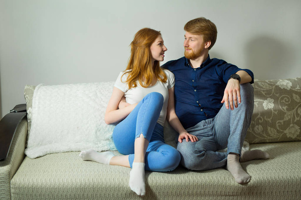 beautiful young couple guy with a girl with red hair sitting on the couch - Фото, зображення