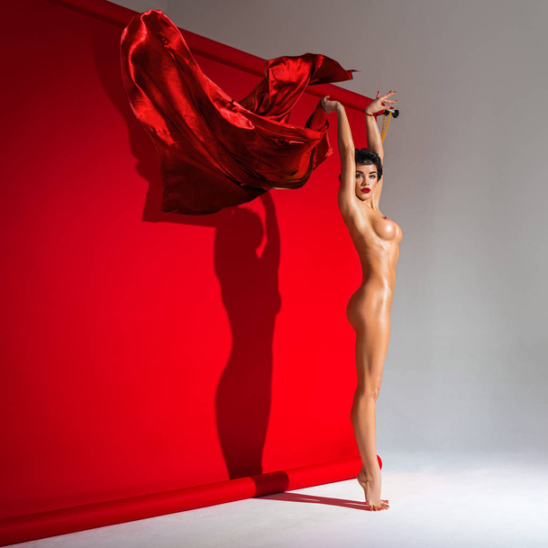 Beautiful Naked Woman With Perfect Body Dancing With Red Silk Fabric Isolated On The Red And Gray Background Casting Shadow - Фото, изображение