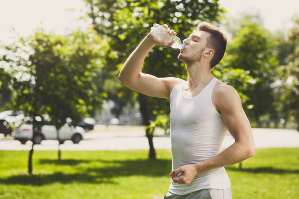 Fitness man drinkwater in park otdoors - Foto, afbeelding