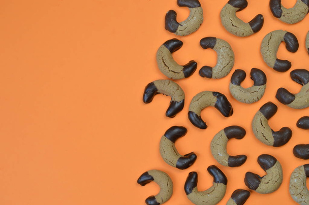 grens uit zelfgemaakte nougat halve manen koekjes met chocolade op de randen en de kopie ruimte aan de linkerkant op een oranje achtergrond - Foto, afbeelding