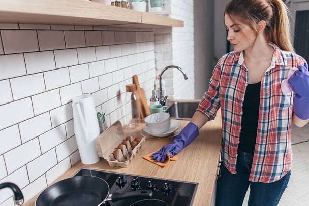 Vrouw in rubberen handschoenen keukentafel schoonmaken. - Foto, afbeelding