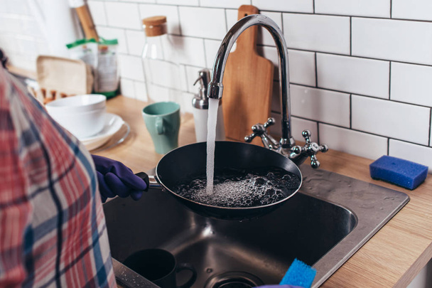 Young woman wearing rubber gloves washing frying pan in kitchen - Foto, immagini