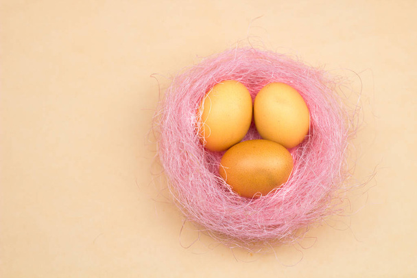 Пасхальные желтые яйца в розовом гнезде на желтом фоне. Крупный план в стиле минимализма
. - Фото, изображение