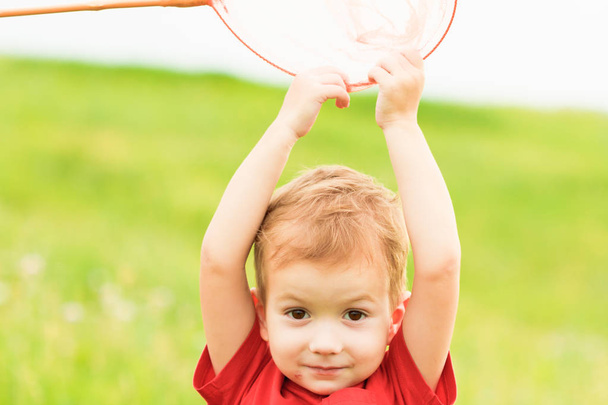 Adorable Caucasian kid playing with scoop-net on the meadow on warm and sunny summer or spring day. - Foto, Imagen