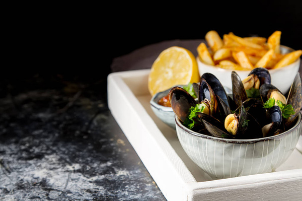 Mussels with herbs in a bowl with lemon and French fries on a wh - Fotografie, Obrázek