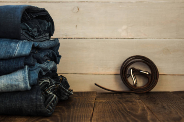 A stack of jeans on a wooden background and a belt - Fotó, kép