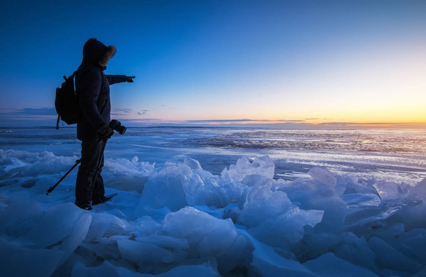 写真家は、日没時に凍った川で写真を撮る.  - 写真・画像