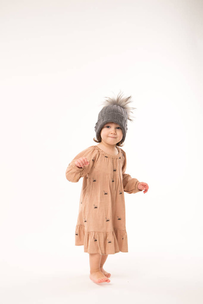 Cute little girl in beige dress in a gray hat isolated on white background. - Foto, imagen