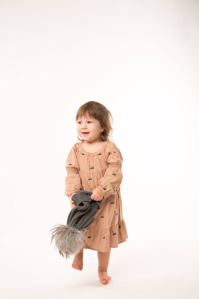 Cute little girl in beige dress in a gray hat isolated on white background. - Zdjęcie, obraz