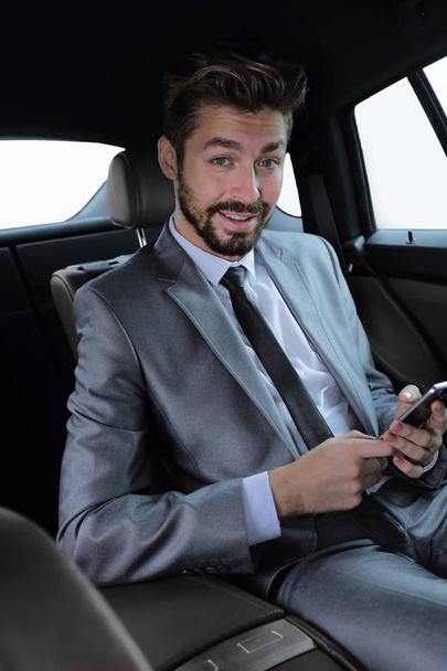 man in suit sitting in car and reading messages on smartphone - Фото, изображение