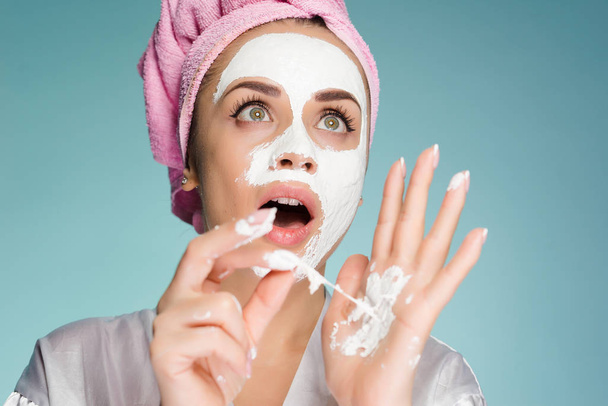 an amazed woman with a towel on her head after showering apply a cleansing mask on her face - Foto, Imagen
