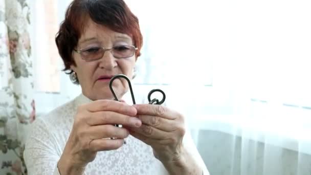 An old woman unravels a metal puzzle, coaches brain activity - Footage, Video
