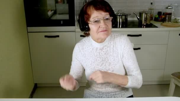 eine ältere Frau hört über Kopfhörer Musik aus dem Telefon, gestikuliert energisch und tanzt - Filmmaterial, Video