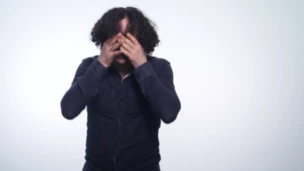 Portrait of an attractive young man with curly hair turns her head looking into the camera on white background - Imágenes, Vídeo
