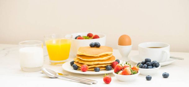 ブルーベリーとストロベリー ブラック コーヒーと、パンケーキとグラノーラの健康的な朝食セット、ミルク、オレンジ ジュース白い石のテーブル背景 - 写真・画像