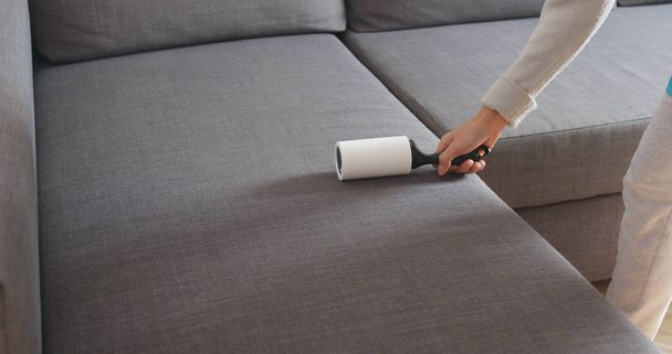 Woman with sticky roller cleaning sofa  - Photo, Image