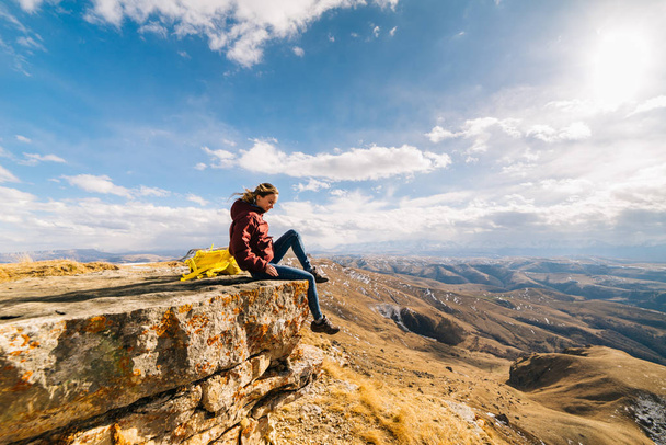 woman tourist sits on the edge of a cliff in the background of mountains - Fotoğraf, Görsel