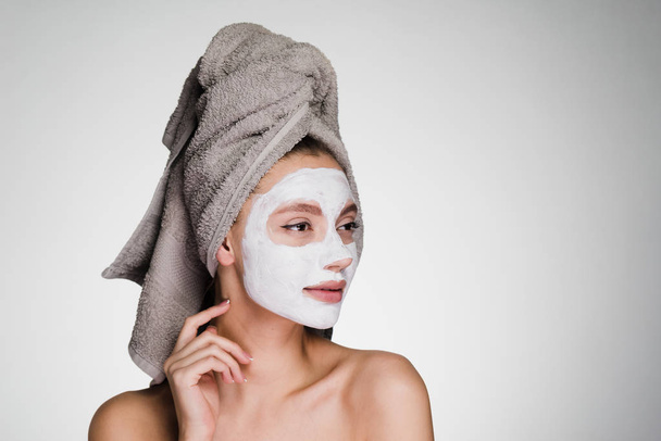 pensive woman with towel on her head after shower apply cleansing mask on face - Foto, afbeelding