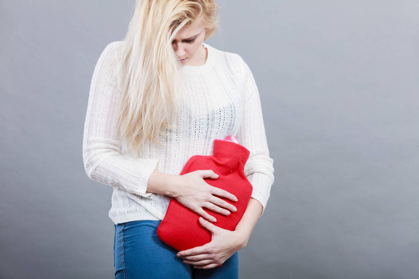 Woman feeling stomach cramps holding hot water bottle - Fotó, kép