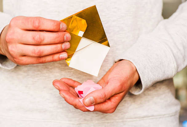 Γυναικεία χέρια κρατώντας χρυσό χαρτί φάκελος με καρδιές. Άνοιγμα φακέλου χρυσό origami - Φωτογραφία, εικόνα