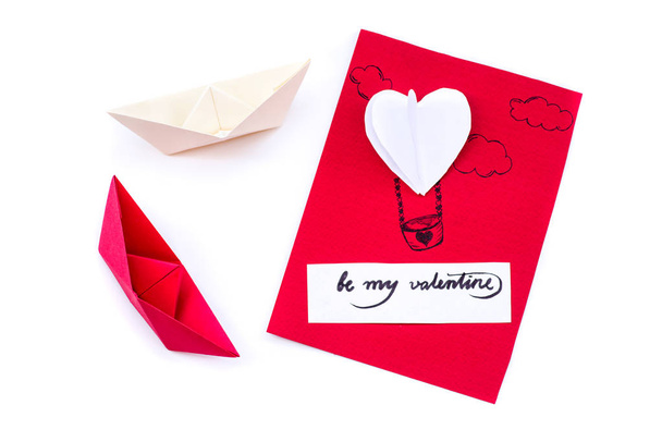 ημέρα του Αγίου Βαλεντίνου διακοπών. χειροποίητο δώρο κάρτα με ένα μπαλόνι καρδιά, μια καρδιά origami και δύο σκάφη χαρτί σε λευκό φόντο - Φωτογραφία, εικόνα