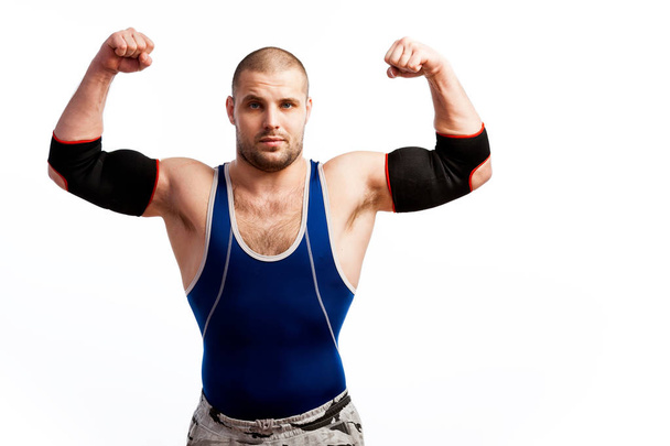 Jeune homme athlétique en collants bleus et coude noir se tient et montre biceps sur fond blanc isolé
 - Photo, image