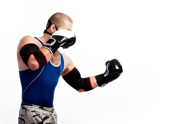 Молодий спортивний чоловік у синіх колготках, чорна тренувальна маска, чорно-білі боксерські рукавички та чорні лікті боксу на білому ізольованому тлі, вид збоку
 - Фото, зображення