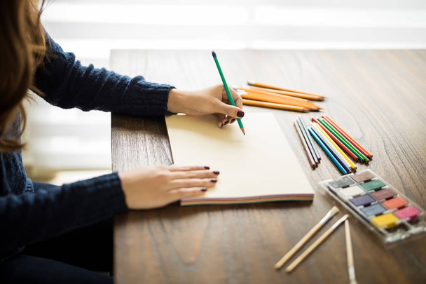 Close up de mãos pintoras desenhando esboço em caderno de esboços usando lápis com cores de água e lápis de cor deitado em mesa de madeira
. - Foto, Imagem