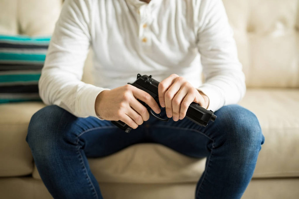 Close up of man with a pistol in hand sitting on couch - Foto, Imagem