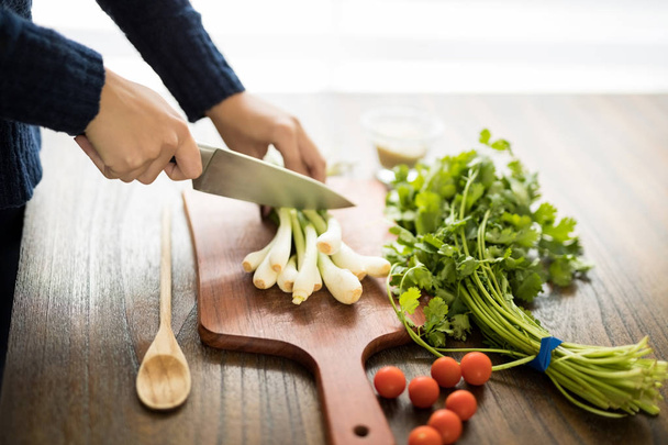 Primer plano de las manos de la mujer cortando verduras frescas en la tabla de cortar con cilantro y tomates en la mesa de madera
 - Foto, imagen