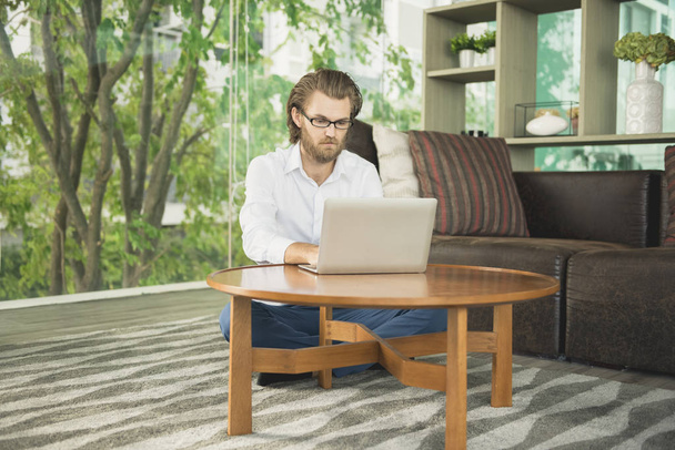 Empresario occidental estresado usando un ordenador portátil en la sala de estar
 - Foto, imagen