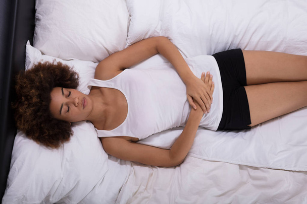 Young Woman Suffering From Stomach Pain Lying On Bed In Bedroom - Photo, image