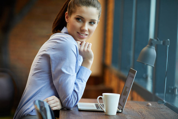 Portrait of a happy casual businesswoman sitting at her workplace in office - 写真・画像