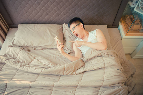 Θυμωμένος άνθρωπος Ασίας κατηγορούμε σχετικά με το τηλέφωνο στο κρεβάτι - Φωτογραφία, εικόνα